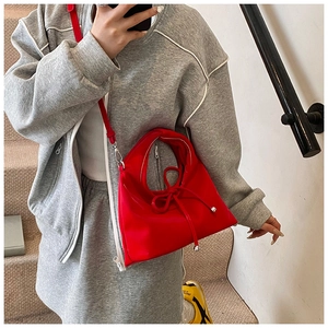 Close-up of red hobo bag with large silk bow detail worn by model in casual grey set