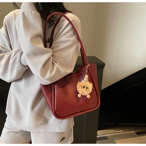 Detail of burgundy leather tote bag with yellow plush charm on model's shoulder