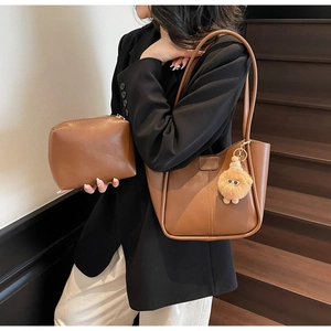 Detail of a brown leather tote bag with a small matching pouch and plush monster charm