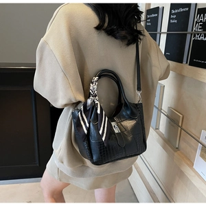 Close-up of black crocodile-embossed handbag with elegant silk scarf and silver twist lock