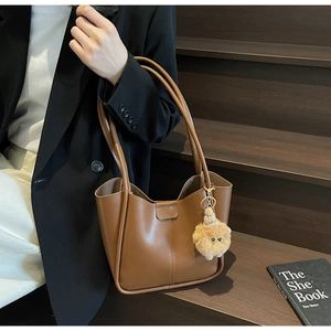 Close-up of caramel faux leather tote bag with stylish plush bear charm detail