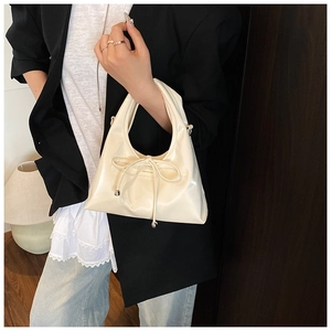 Detail of a creamy white bow handbag with NOFILTER logo and glossy PU leather texture