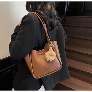 Close-up of brown matte leather tote bag with long strap and plush monster charm