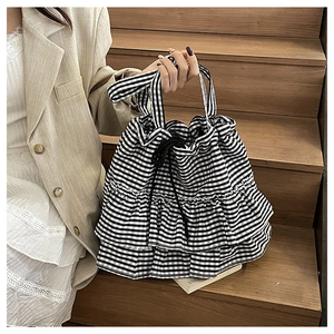 Detail of checkered tote bag featuring ruffle trim and drawstring closure in stylish canvas