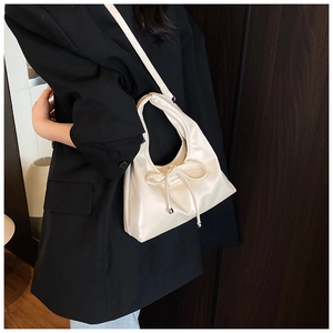 Detail of a beige leather shoulder bag with a decorative bow and metallic beads