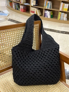 Minimalist black crochet tote bag with hollow rhombus pattern on a rattan chair
