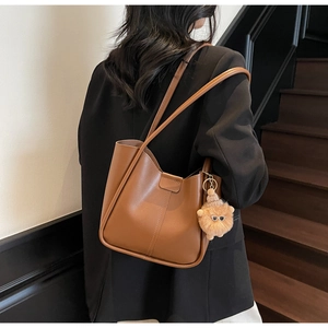 Brown faux leather tote bag close-up with a cute plush monster charm and smooth texture