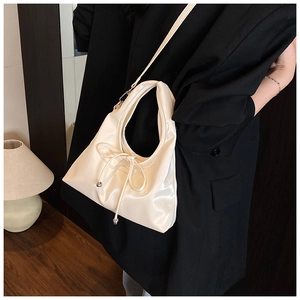 Close-up of cream white glossy leather shoulder bag with bow knot on black blazer