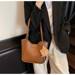 Brown leather tote bag featuring a cute plush charm accessory for trendy daily commuting
