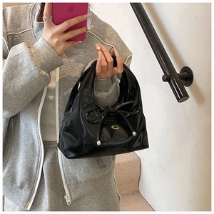 Detail of a small black patent leather handbag featuring a bow and silver hardware