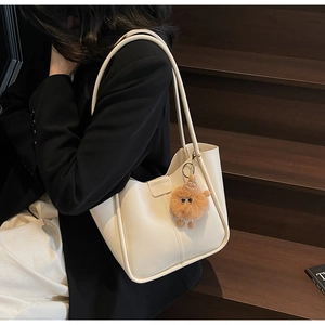 Chic cream tote bag with brown plush pendant shown on model against wooden stairs