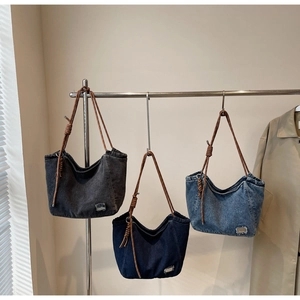 Detail view of denim tote bag with thick brown woven rope strap and chic metallic decor
