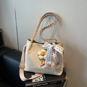 Dettaglio borsa tote in paglia con manici intrecciati, sciarpa di seta e ciondolo a fiore