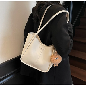 Close-up of creamy white leather tote bag with fine textures and plush monster pendant