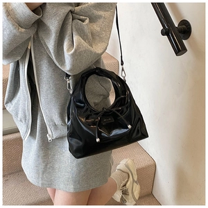 Detail of black patent leather bucket bag with bow drawstring and silver metal beads