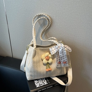 Dettaglio della borsa tote in paglia intrecciata con ciondolo a fiore e foulard di seta