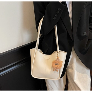 Detail view of cream leather tote bag with brown lion plush charm on a black blazer outfit