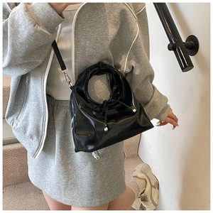 Detail of a black patent leather bucket bag with metal ball drawstring and round handle