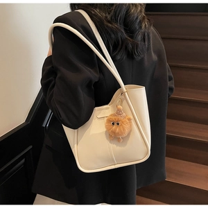Minimalist beige leather tote bag with brown plush monster charm on a female model