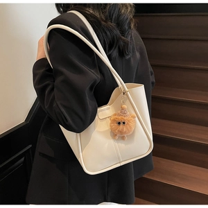 Minimalist cream tote bag with stylish plush pendant shown on a model in urban style