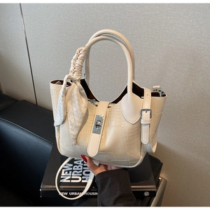 Detail of cream croc-effect bucket bag featuring gold metal turn-lock and silk ribbon