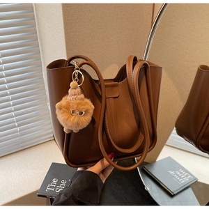 Detailed shot of brown leather tote bag with a cute plush charm and adjustable straps