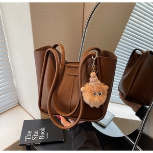 Detail of a brown leather tote bag featuring a cute furry charm and textured surface