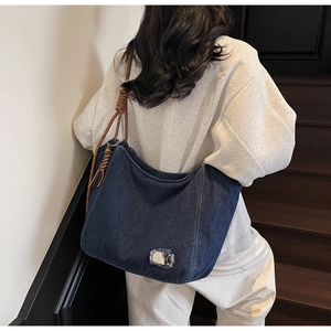 Close-up of denim tote bag featuring fringe details and brown braided rope shoulder strap