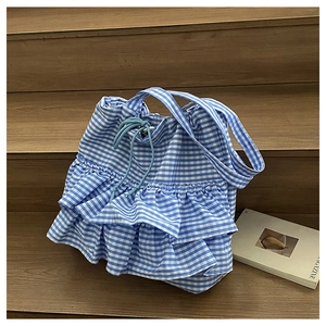 Detail of blue gingham tote bag showing ruffle trim and drawstring closure on stairs