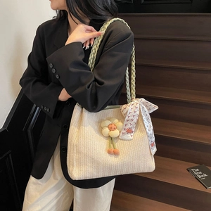 Dettaglio della borsa tote intrecciata beige con ciondolo a fiore e foulard in seta