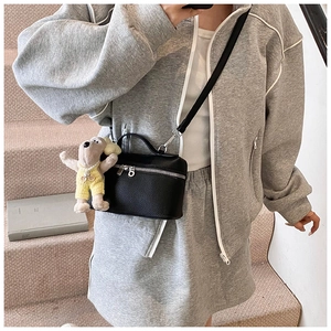Detail of black litchi grain leather box bag featuring a cute puppy plush charm accessory