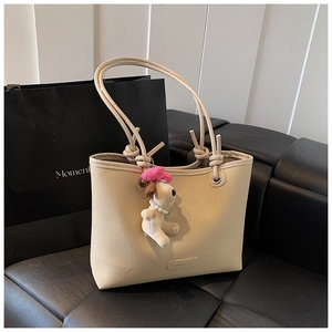 Detail of cream tote bag with pebble leather texture, metal ring and plush dog charm
