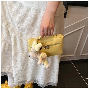 Detail of yellow lychee leather box bag with cute puppy charm and metallic dual zippers
