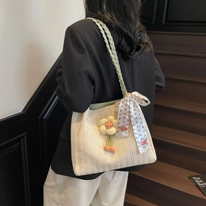 Dettaglio della borsa tote in paglia con manici verdi, foulard di seta e ciondolo a fiore
