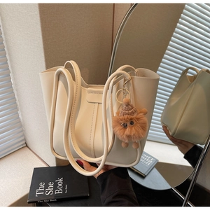 Detail of cream leather tote bag with a plush monster charm in a minimalist room