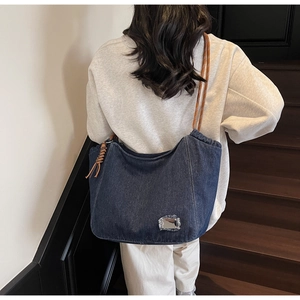 Detail of dark blue denim tote bag featuring braided brown rope strap and leather tassel