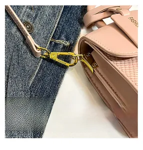 Detail of pink crossbody bag showing gold buckle and woven texture on a denim backdrop