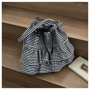Detailed view of black and white gingham bucket bag with ruffles on a wooden staircase
