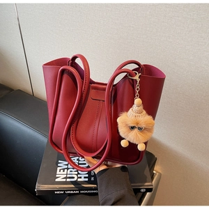 Detail view of burgundy leather tote bag with plush charm on a luxury leather couch