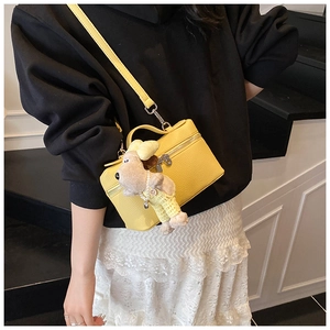 Detail of yellow lychee leather box bag with cute dog pendant and adjustable strap