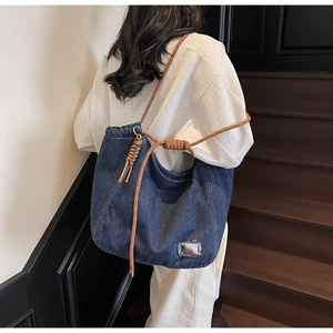 Detail of blue denim tote bag with brown braided rope handles and distressed texture