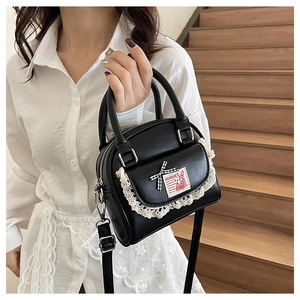 Detail of black leather shell bag with white lace trim and plaid bow on wooden stairs