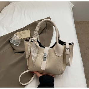 Detailed view of beige crocodile embossed bucket bag with decorative handle scarf and metal lock