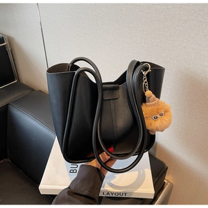 Detail of black leather tote bag with a whimsical fuzzy monster charm on the handle