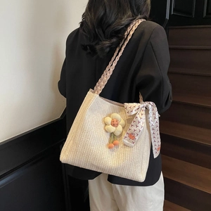 Dettaglio della borsa tote in paglia con manici rosa, fiore di peluche e foulard di seta