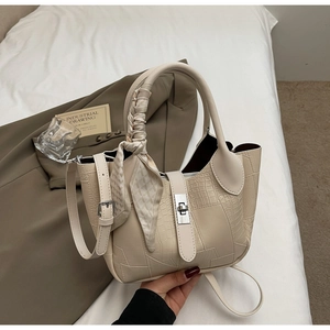 Close-up of stone texture handbag featuring silver twist lock and scarf wrapped handle