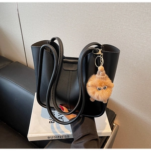 Detail of a black leather bucket bag with a cute plush charm on a business book