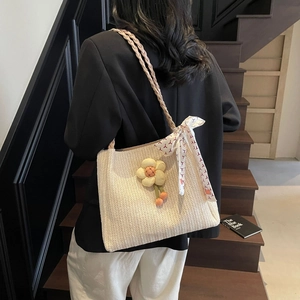 Dettaglio borsa tote in paglia intrecciata con ciondolo a fiore e sciarpa di seta