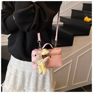 Detail of pink lychee leather box bag featuring a cute plush puppy charm on the zipper