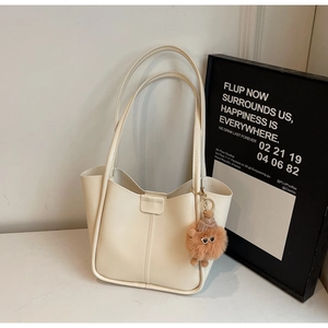 Detail of minimalist cream tote bag with dual handles and brown plush monster charm